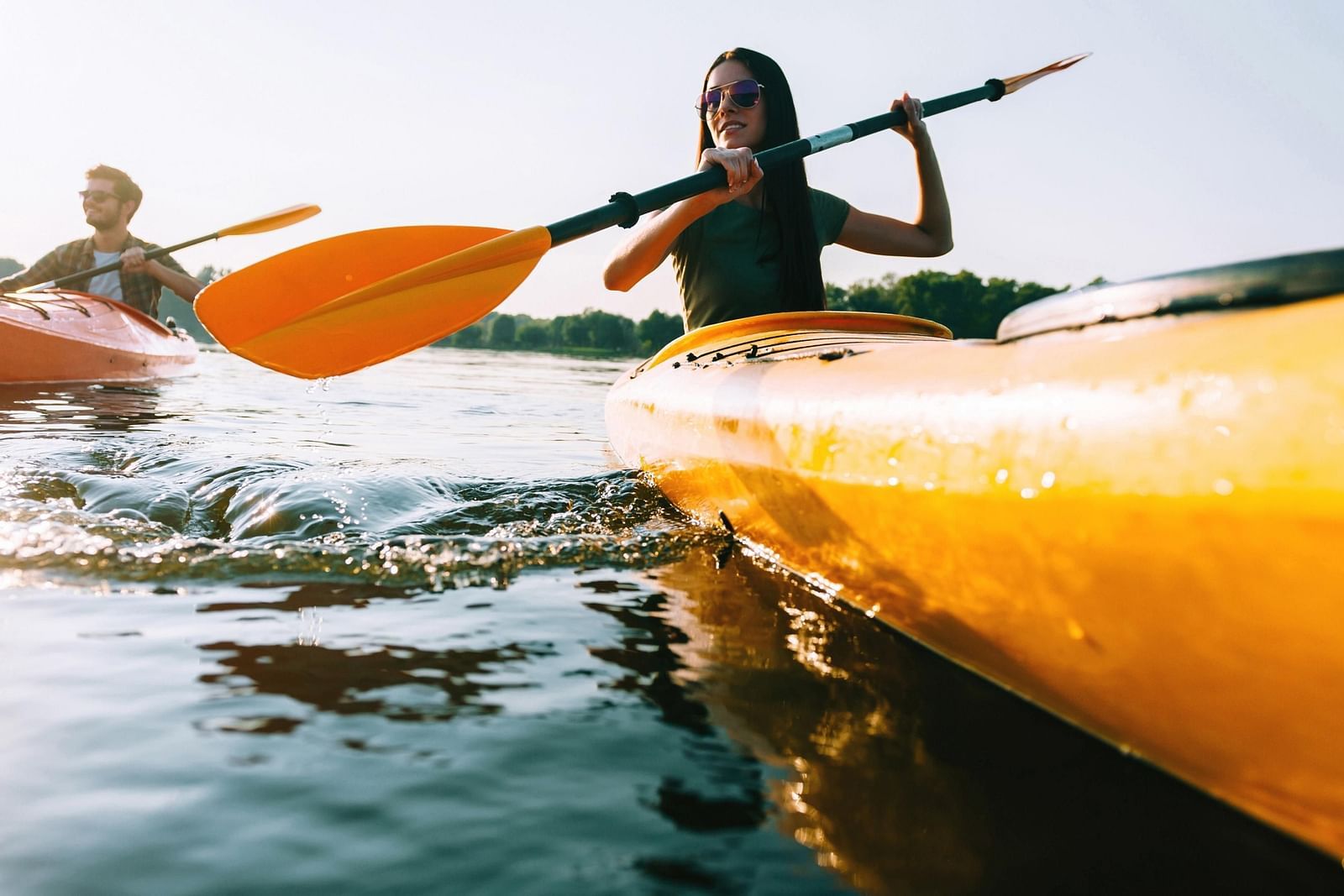 A close up shot of two people kayaking in a waterbody while the sun's ray's hitting the water.