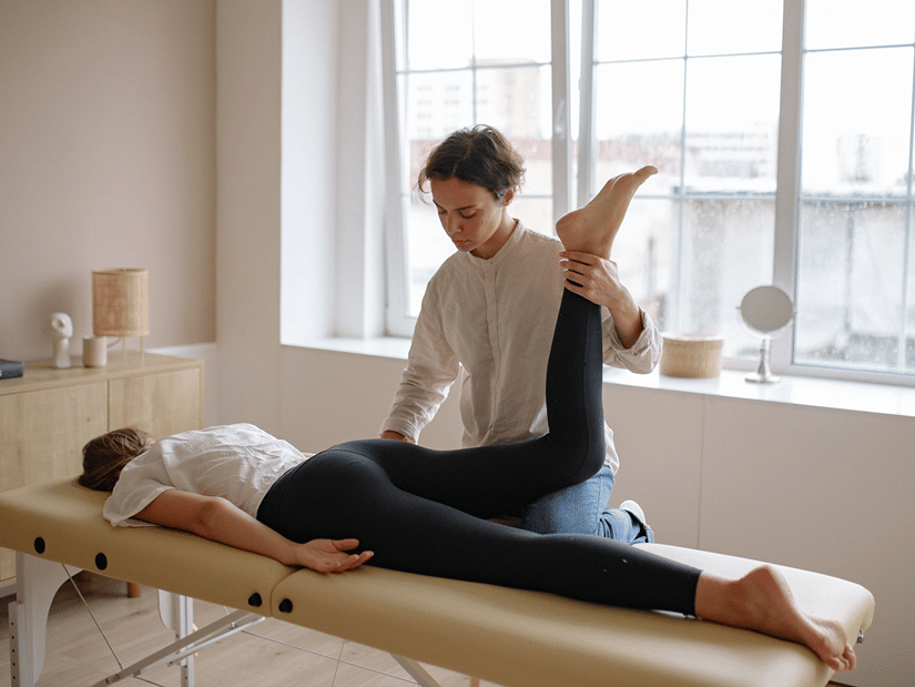 A therapist stretching the leg of a woman lying face down on a treatment table