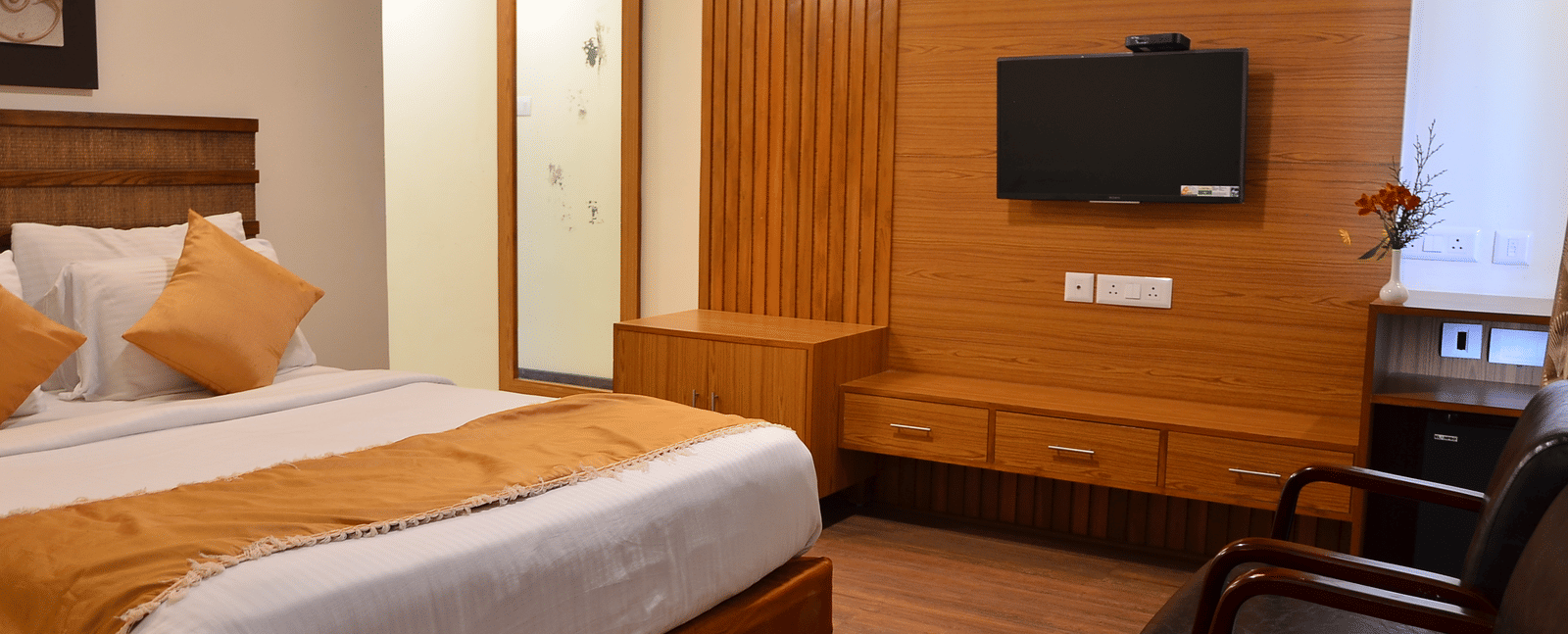 An elegant room with a queen bed, wooden furnishing, and a wall-mounted TV for a relaxing stay - Benzz Park, Kodaikanal