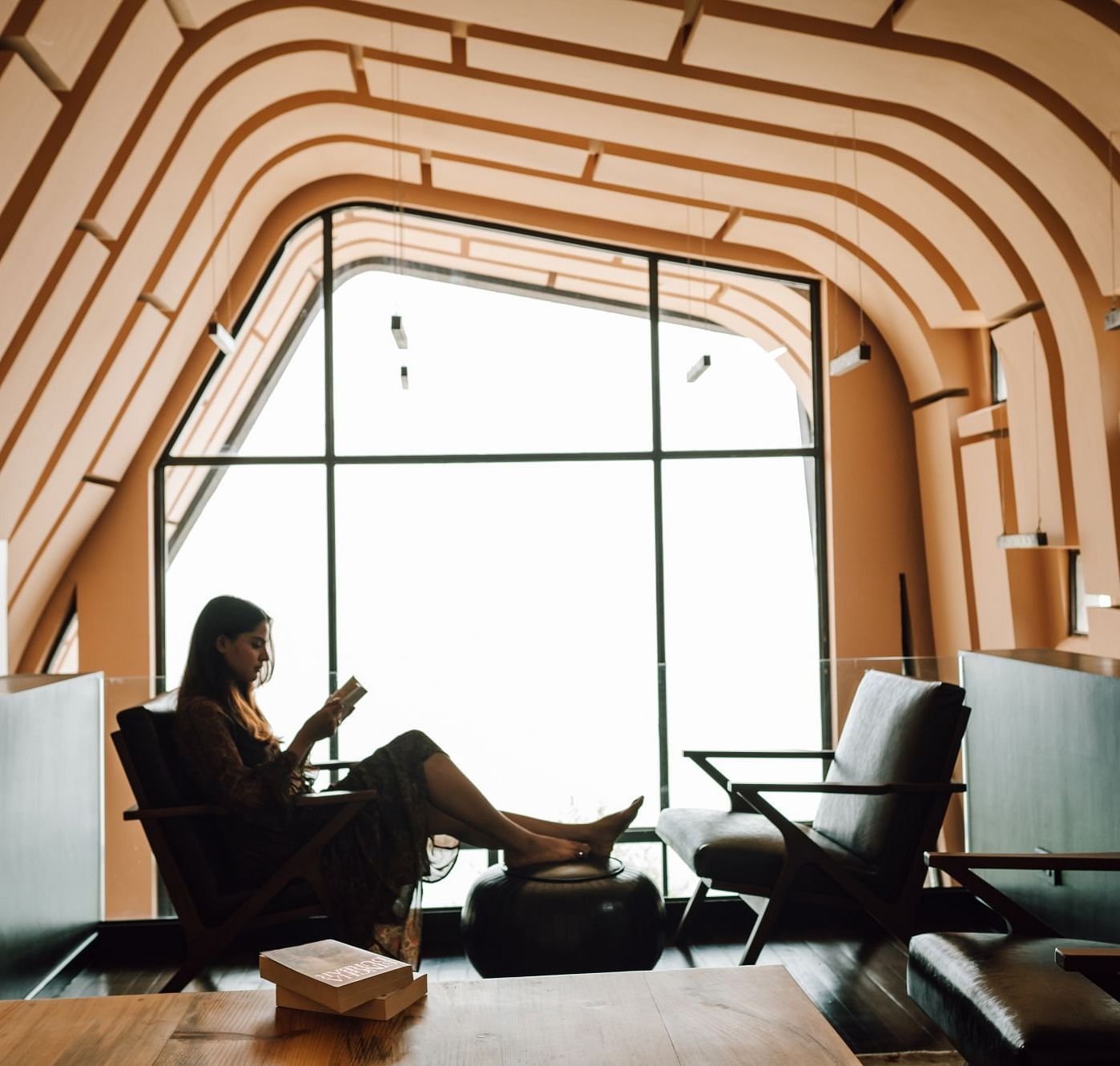 Person reading a book in a stylish, cozy room with unique arched ceiling design.