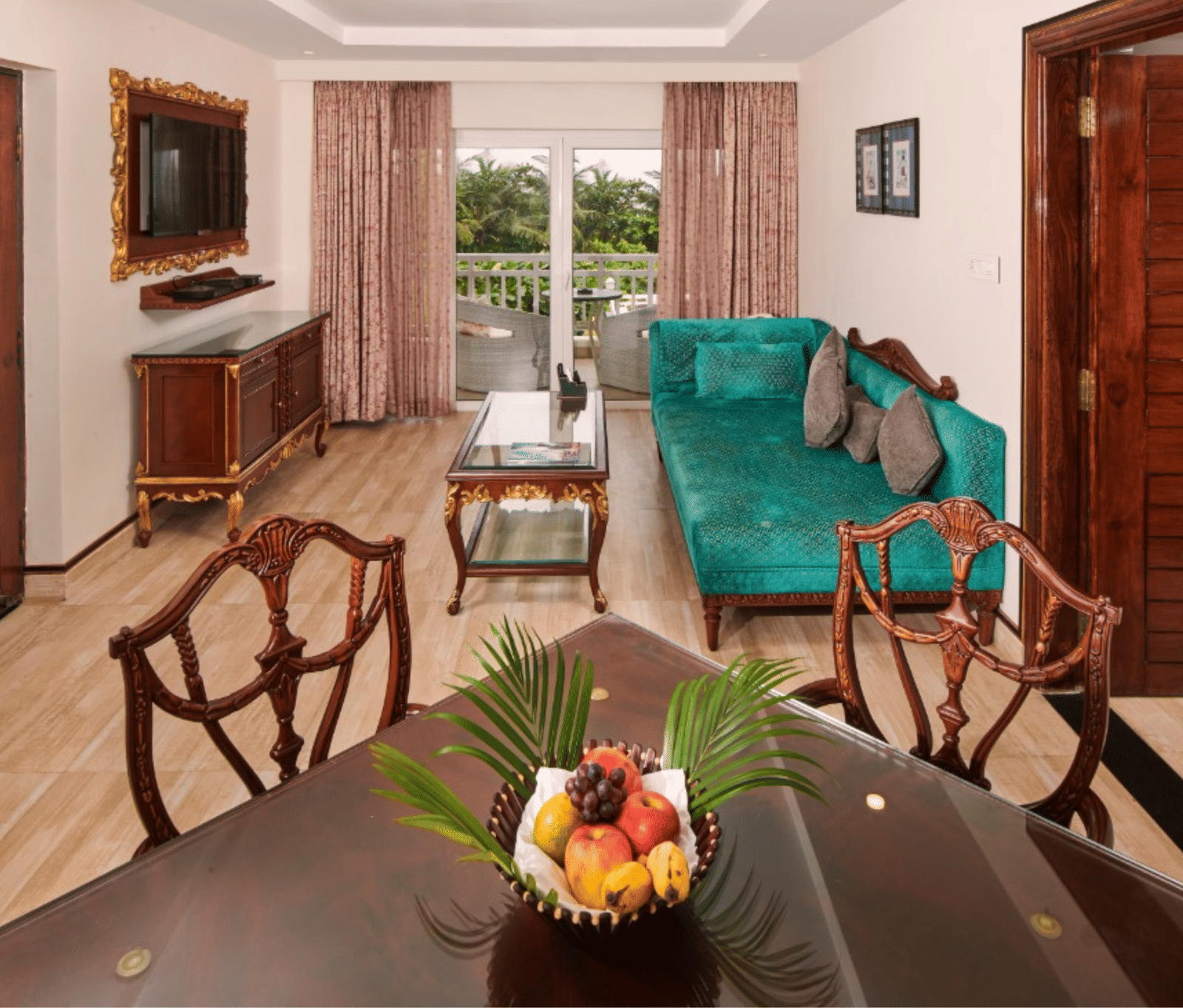 Luxury suite dining and living area at MAYFAIR Heritage Puri, showing wooden table with fruit bowl, teal sofa, and private balcony view.