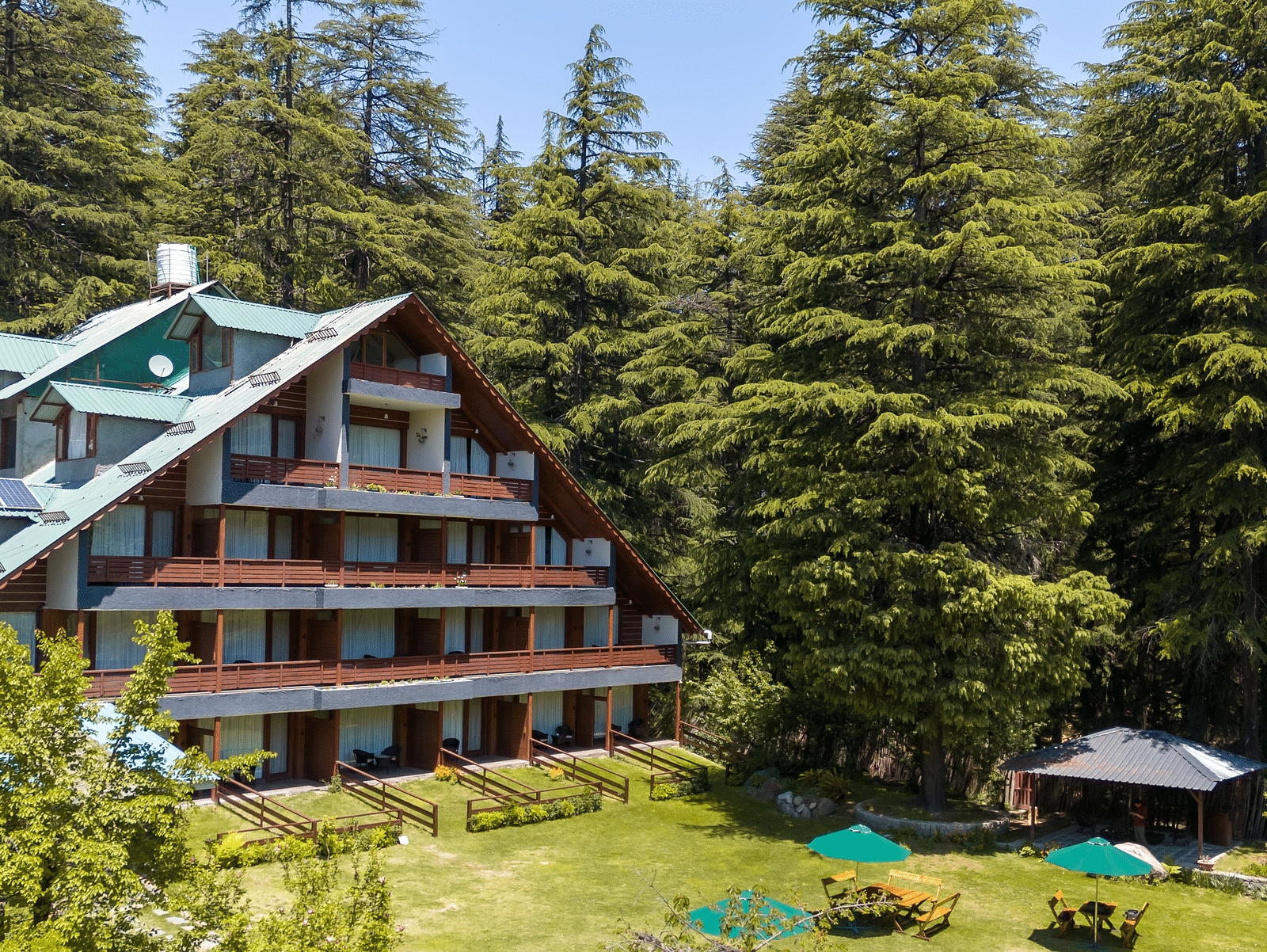 An image of a four storey attic style building set amidst the tall trees - Bedzzz Xclusiv Baikunth, Manali