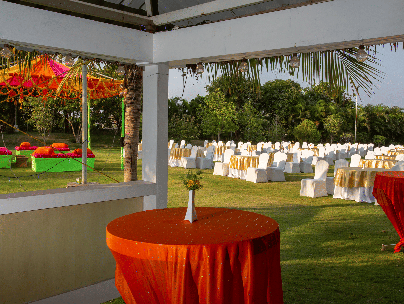 An outdoor event setup with an orange tables under a canopy and white cloth draped chairs in the background - Grande Bay Resort & Spa, Mamallapuram