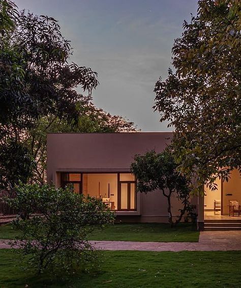 An exterior view of a building with lit windows, surrounded by trees and greenery at dusk - Shreyas Retreat