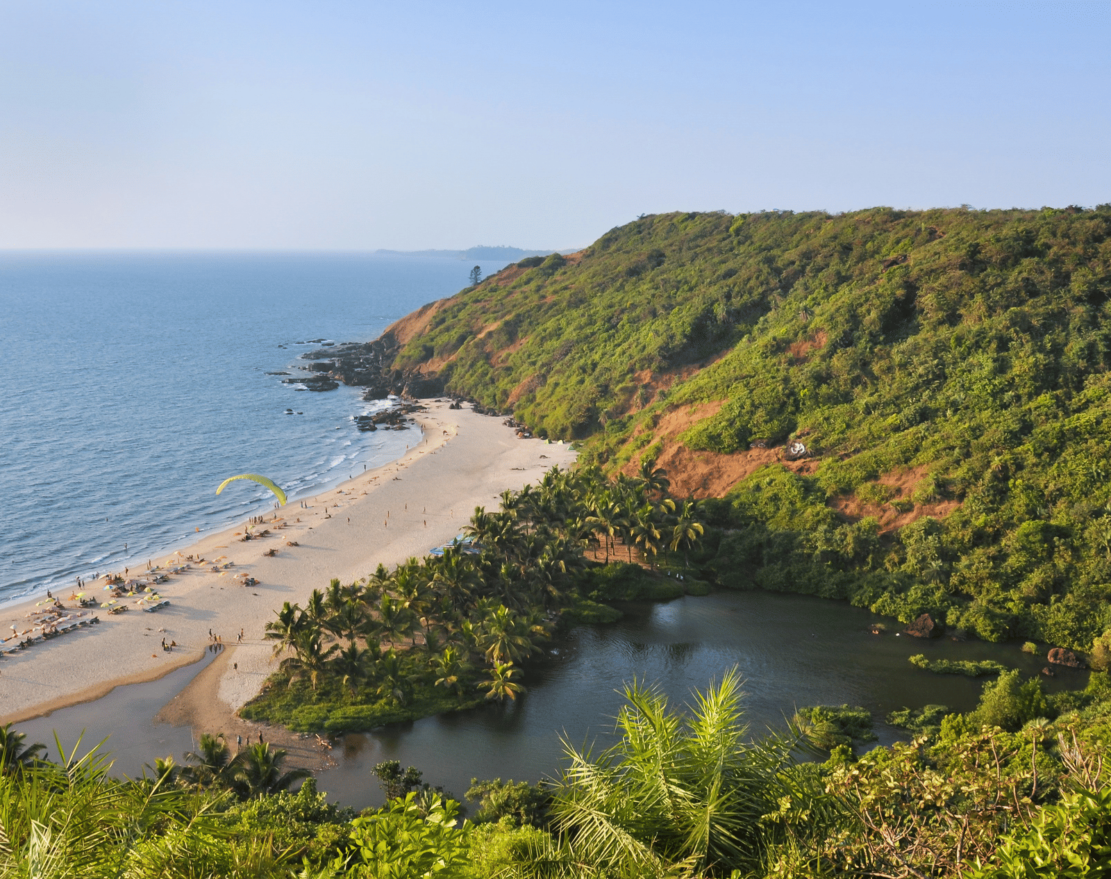 Aerial view of a scenic beach surrounded by a lush green hill in Goa.