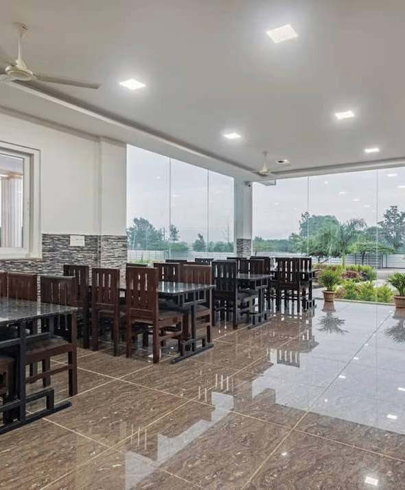 Well-lit restaurant with large windows offering scenic views and comfortable wooden seating at Siri Ambari Resorts and Spa.