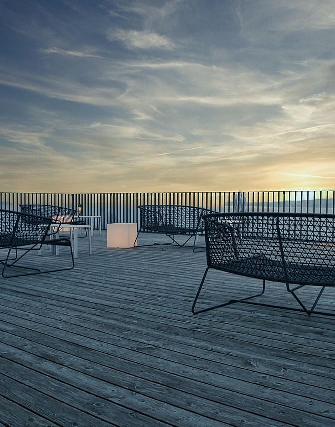 A terrace featuring a wooden deck with a few benches facing towards the beautiful sunset.