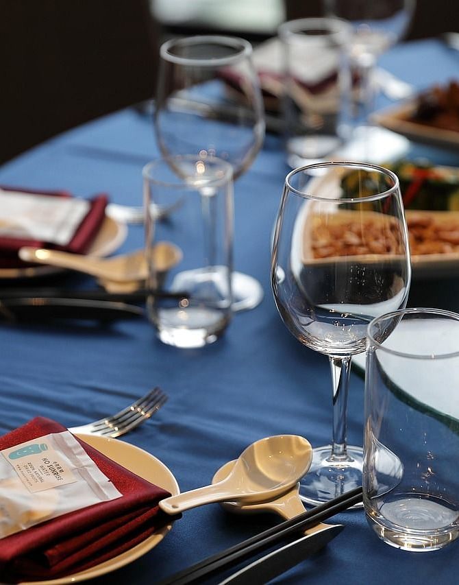 A close up shot of a round dining table with sparkly glassware and cutlery arranged on it.