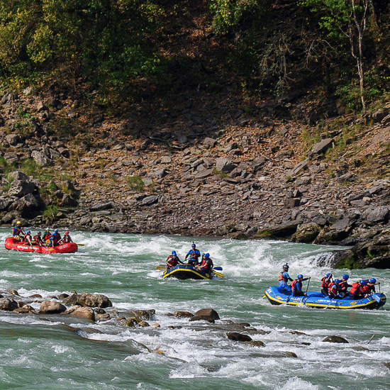 Three blue inflatable rafts filled with people navigating the white water rapids of the river past rocky banks capturing the exciting adventure activities available to guests visiting this riverside retreat