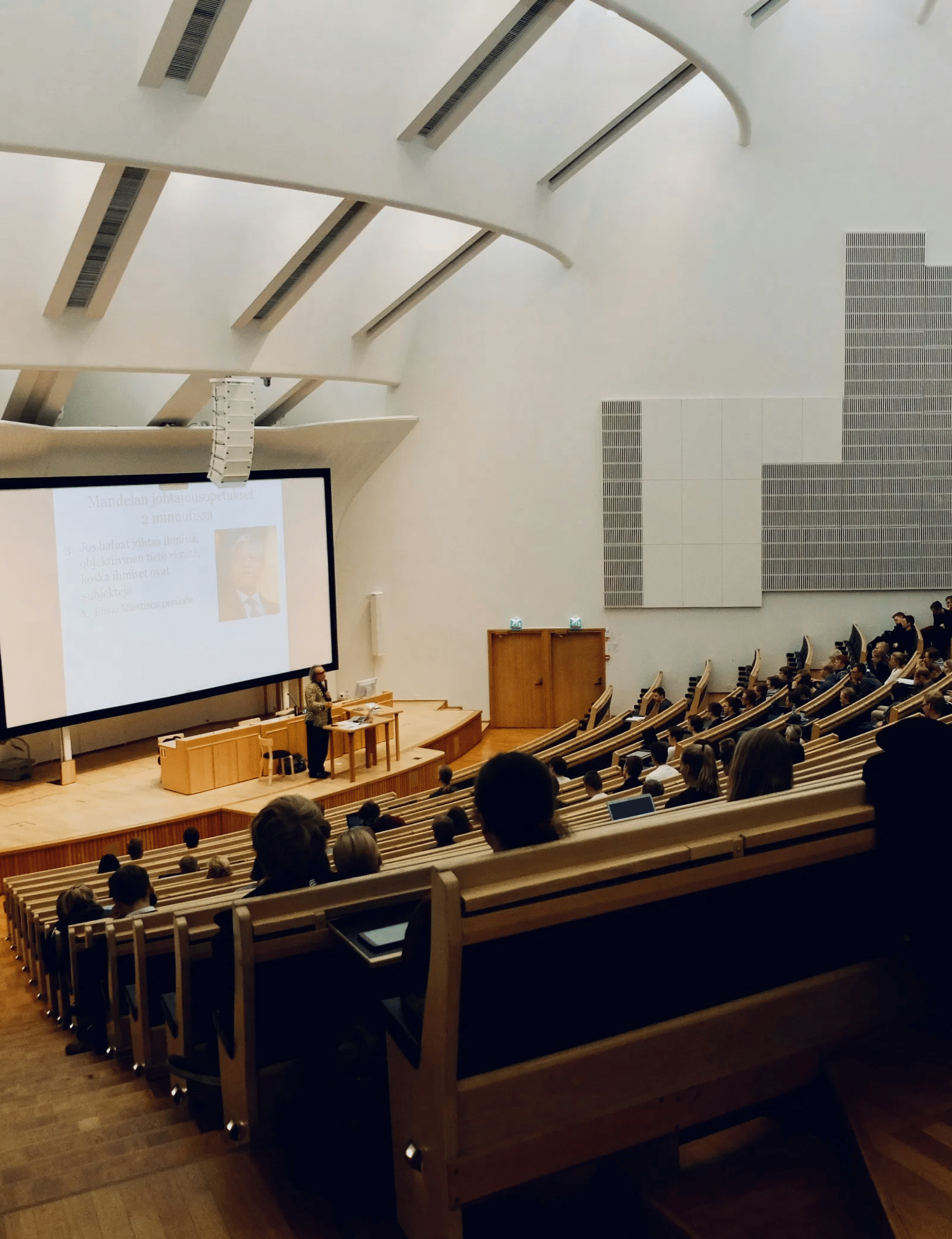 A wide-angle shot of a college classroom with stepped seats facing towards the projector.