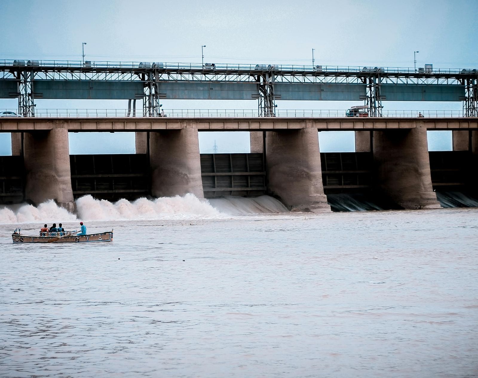 Large dam releasing water with people boating near the base.