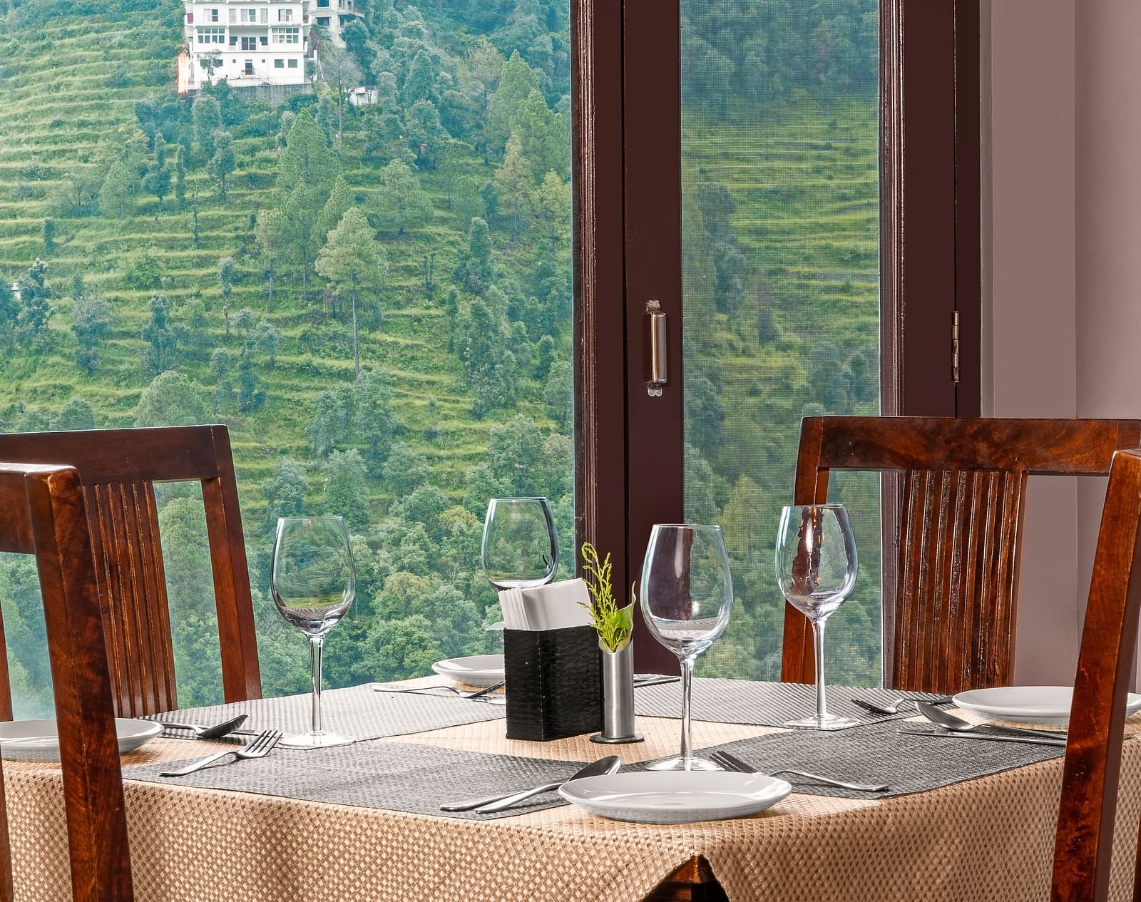 Indoor dining area with a view of terraced hills through large glass windows at BluSalzz Collection - Suvaasa Resort, Ramgarh.