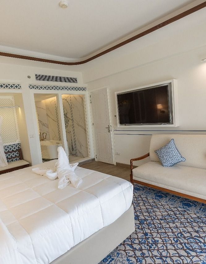 Corner view shot of the bedroom at Ananata Room featuring a plush double bed alon with a television and a couch in front of it at Bhagirathi by RDB Atishay.