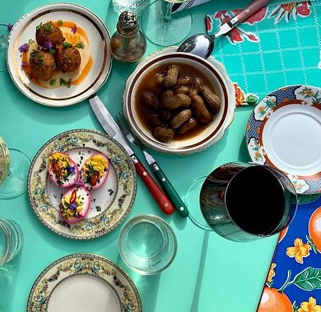 A table is set with plates, bowls, glasses, and utensils, displaying various food items against a patterned tablecloth.
