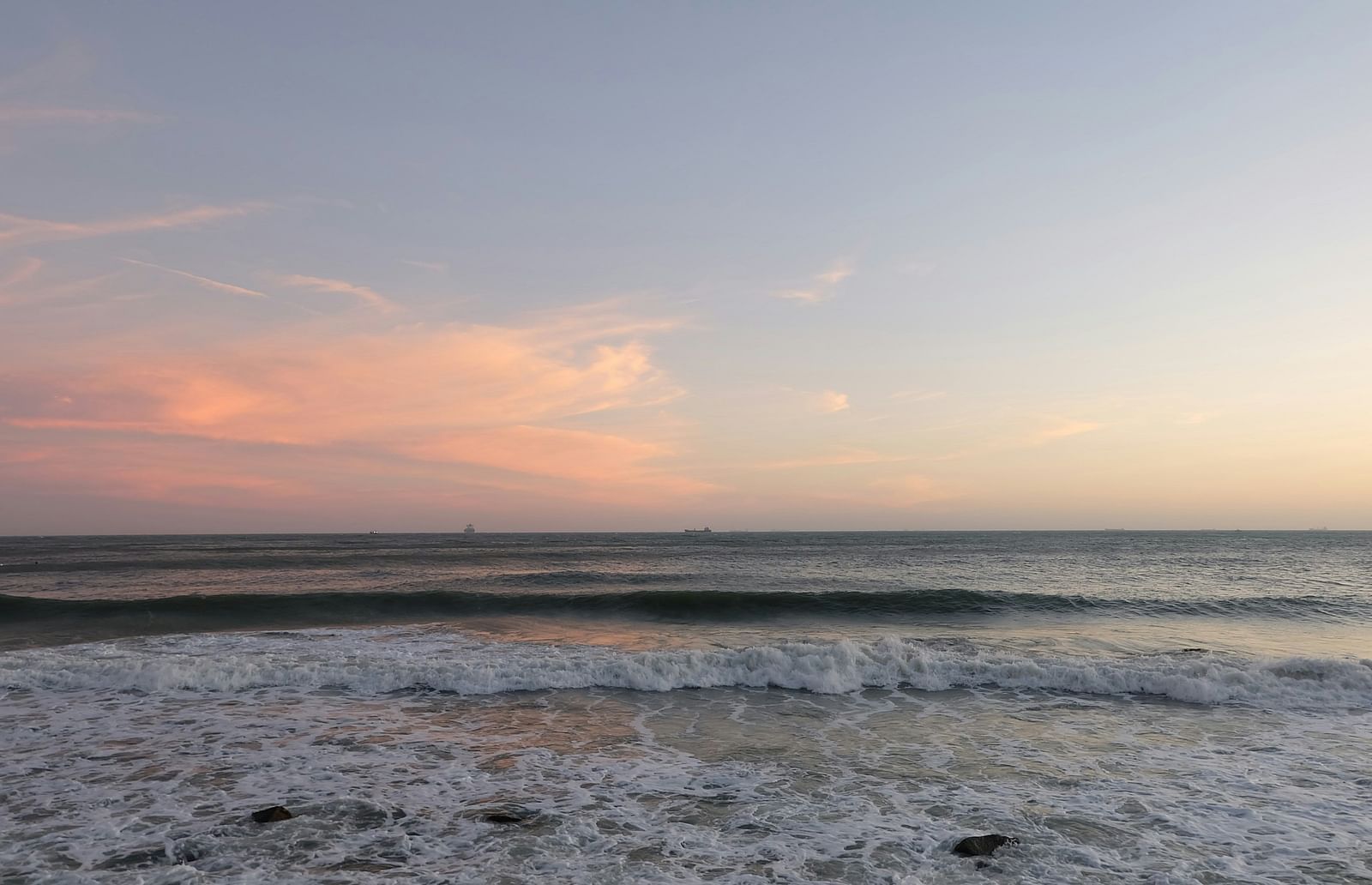 An overview of a beach with waves getting closer and different hues on the clouds in view
