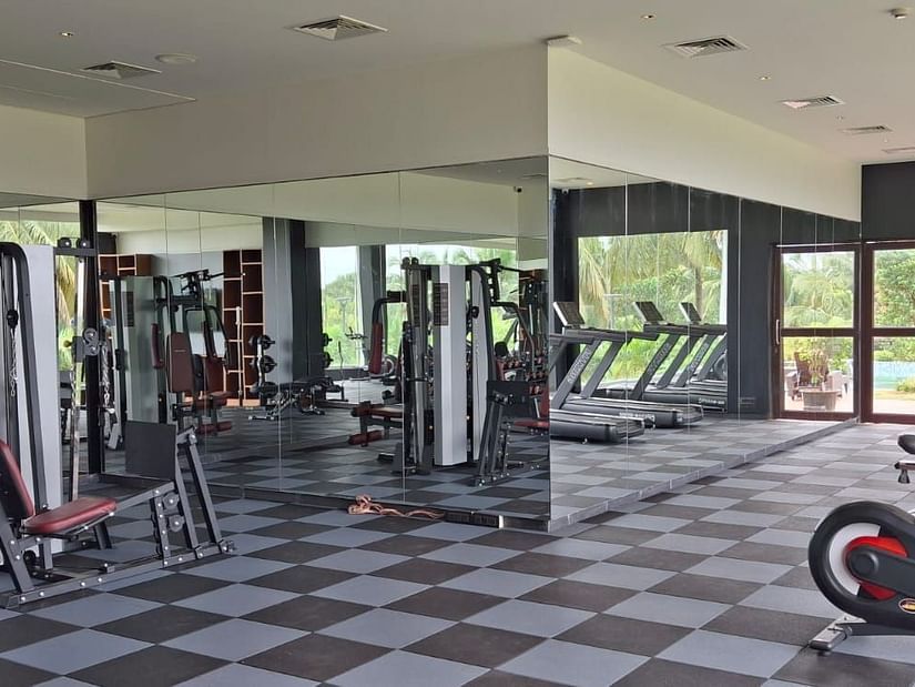 The fitness centre at Cloud9 Sarovar Premiere, Goa, features exercise machines with wall-mounted mirrors and a chess-patterned tile floor, creating an energising and stylish atmosphere