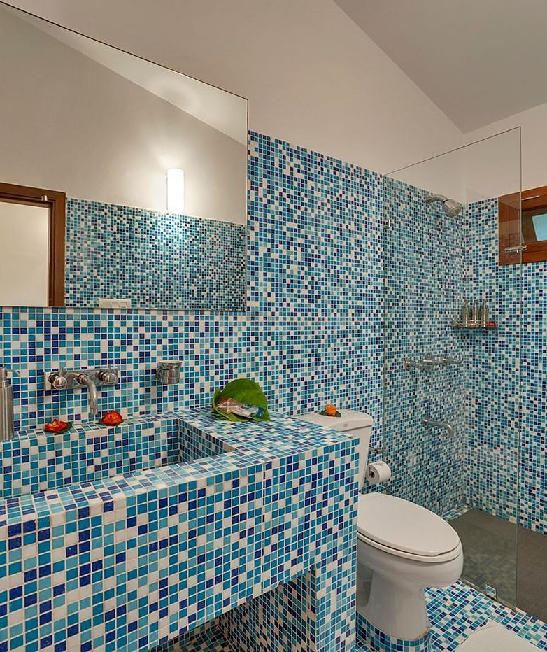 A bathroom with blue mosaic tiles, a toilet, and a sink - Shreyas Retreat