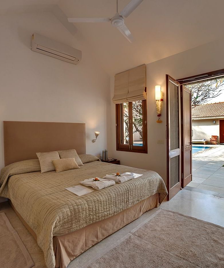 A bedroom featuring a king size bed, warm lighting and a door offering the access to a pool to unwind in - Shreyas Retreat