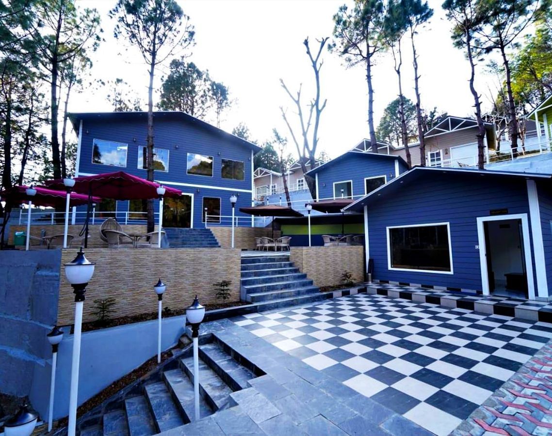 Facade of DLS Nature Trinket Resort, Dalhousie, with a blue building and a clear sky in the backdrop .