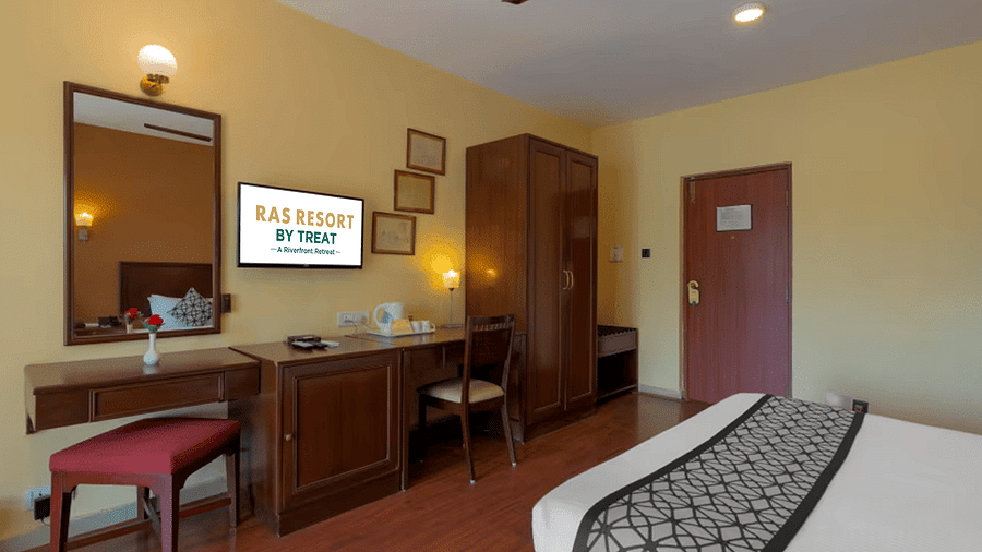 A  room at Ras Resort by Treat, Silvassa, featuring a comfortable bed, a dressing table, and a television with the property logo on it.