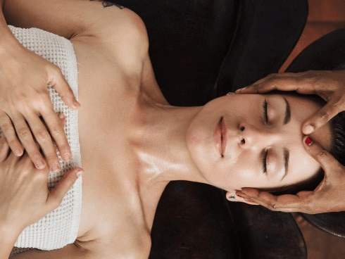 A woman receiving a head massage on a treatment table with her eyes closed