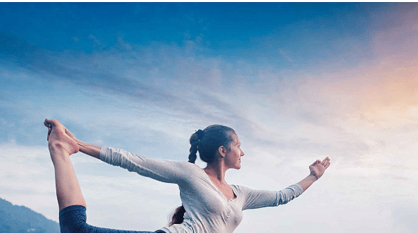 Woman performing a yoga pose at sunrise with serene mountains and sky in the background, promoting International Yoga Day at Aloha on the Ganges, Rishikesh.