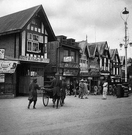 A view of a black and white image with various houses next to each other and people walking in front of it.