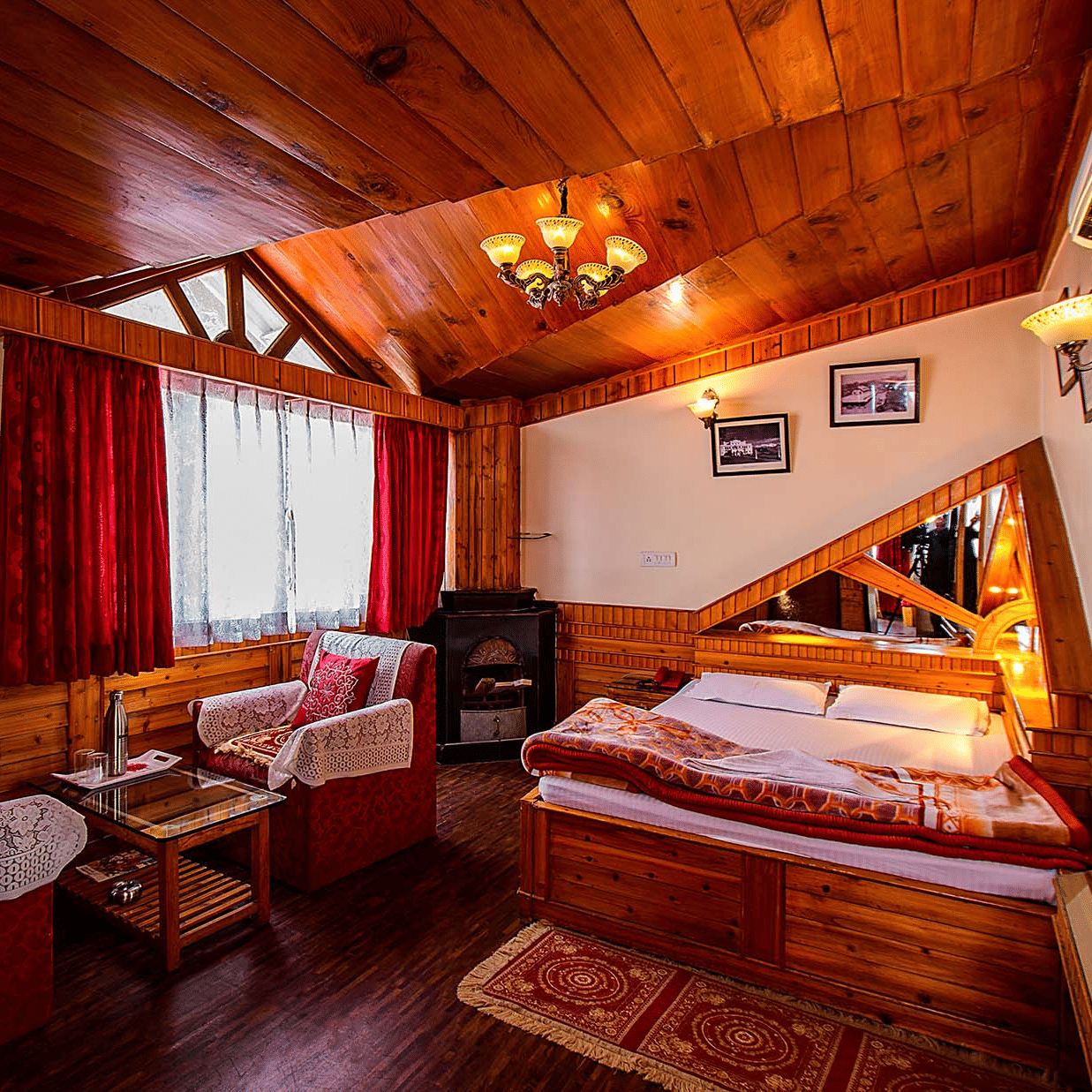 Hotel room with a wooden ceiling, double bed, red and white seating area, and wall mirrors reflecting the room at Hotel Dolphin Darjeeling.