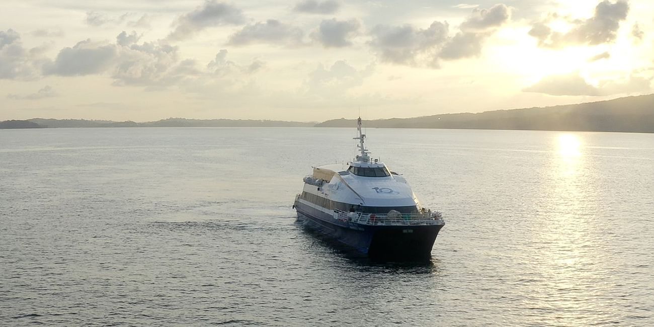A passenger ferry cruising on calm waters during sunset, with the golden sky and distant hills in the background.