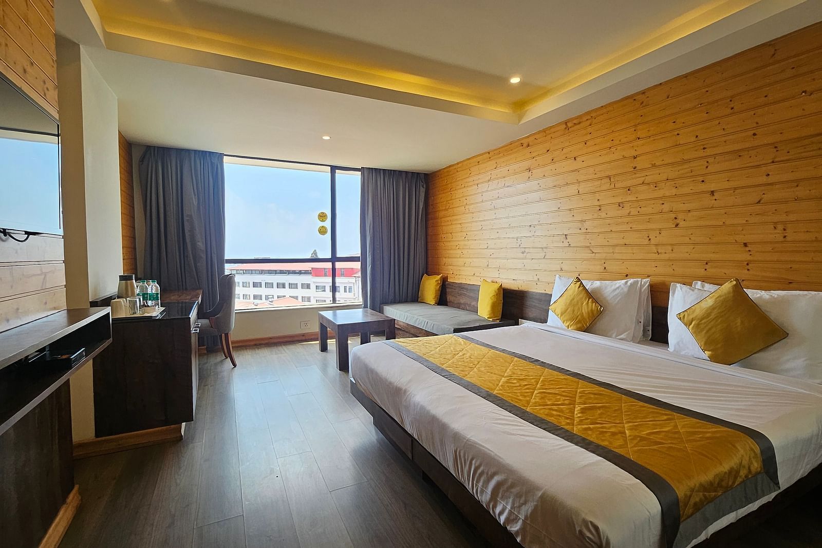 An image of a room featuring a bed, flat screen TV, basic room amenities, and an expansive window overlooking the view - Yashshree Sanderling, Darjeeling