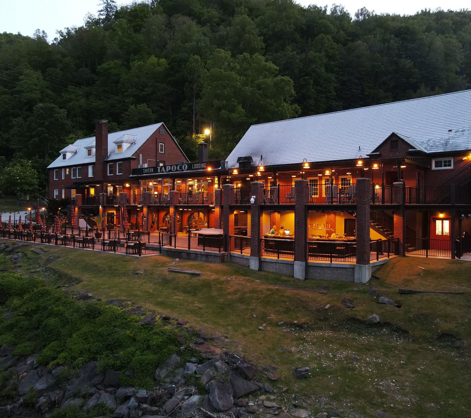 side view of our resort with bright yellow lighting with lush green pine forest in the background - Historic Tapoco Lodge
