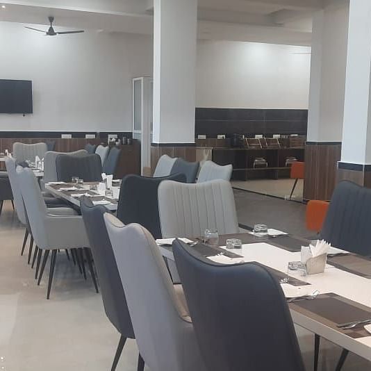 A dining room is arranged with tables and grey chairs, ready for service - Kankidham Lords Inn