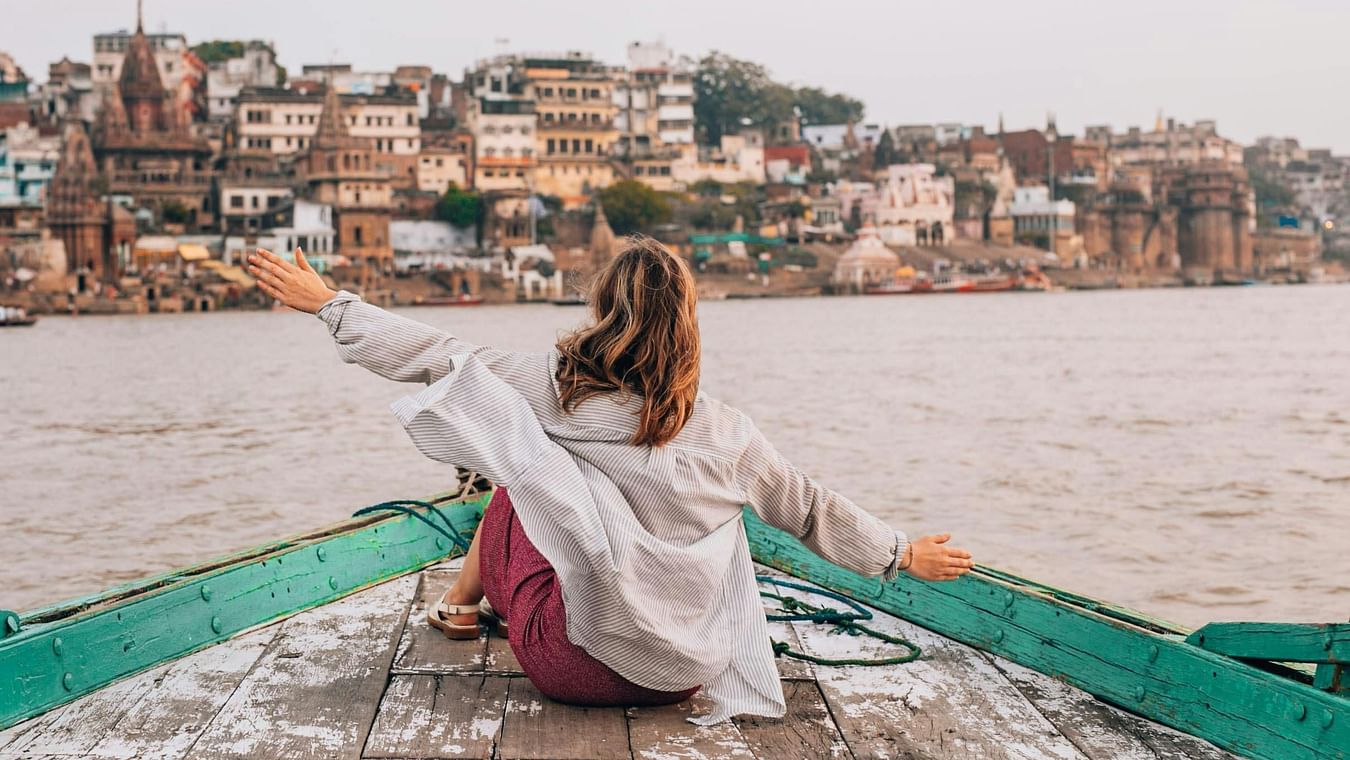 Person in boat on holy river with traditional ghats and ancient city buildings along waterfront