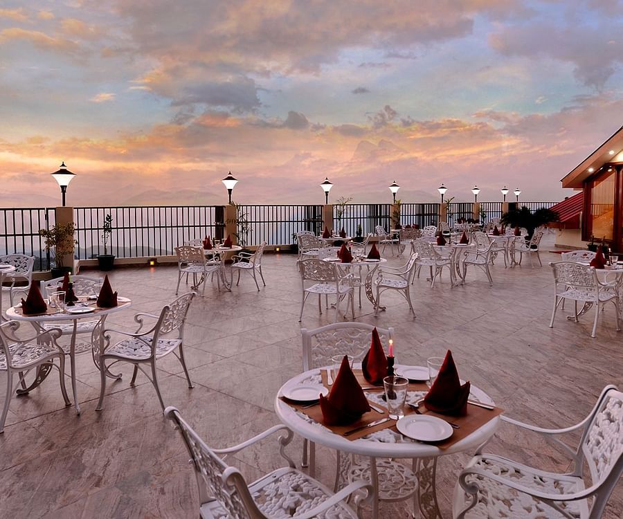 Terrace at JK Clarks Exotica in Dalhousie featuring tables arranged under a colourful evening sky