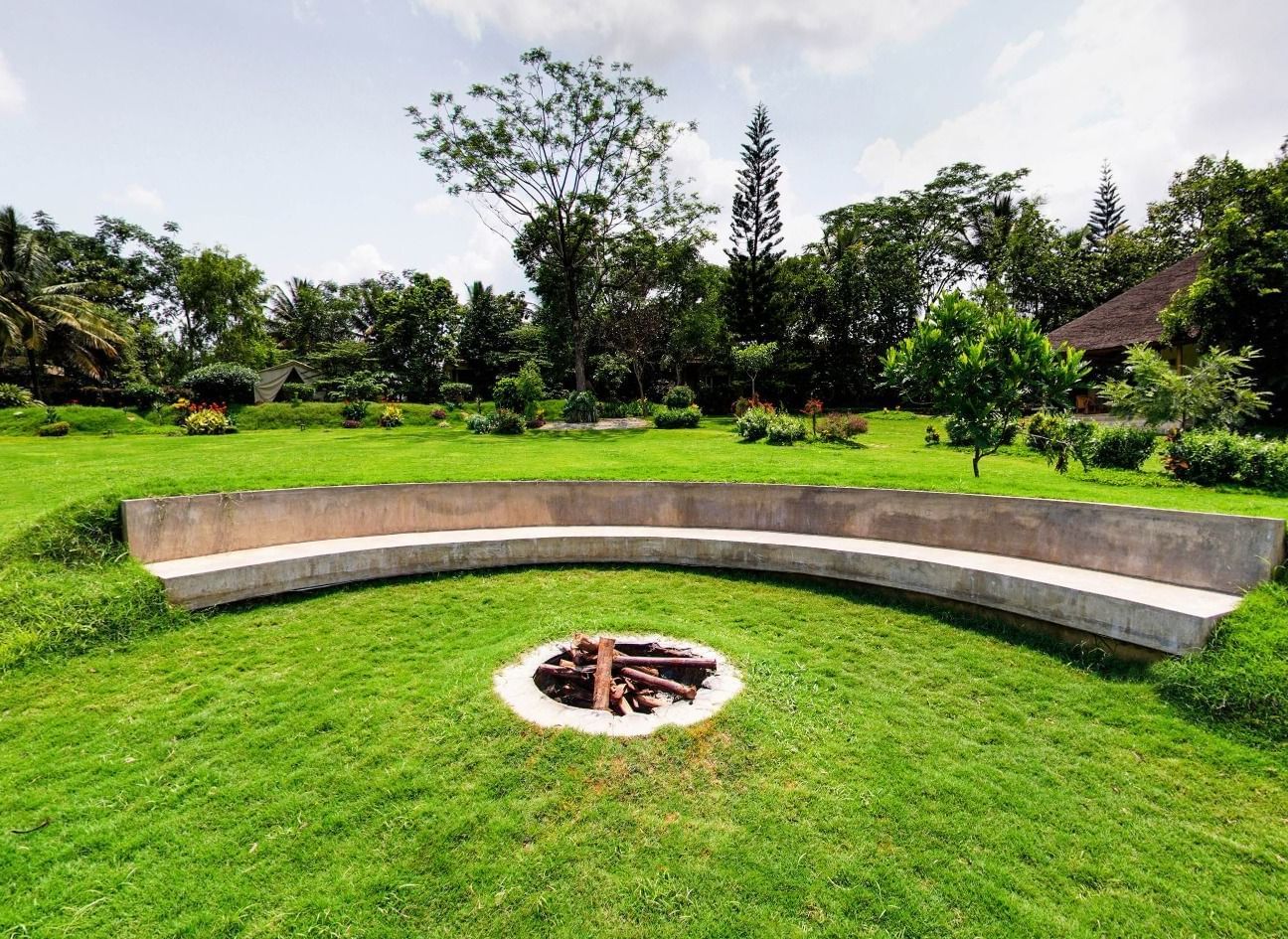 Circular fire pit with curved concrete seating, surrounded by a well-maintained lawn at Fireflies Resorts, Kabini.