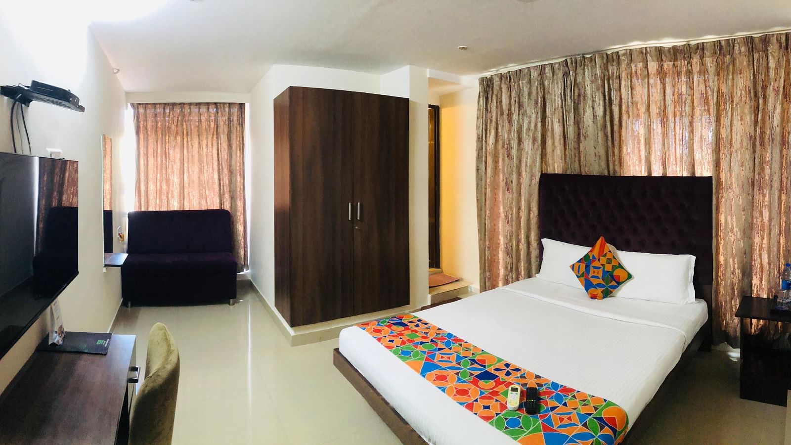 View of Premium Room in Astra Hotels and Suites, HSR Sector 1 where a bed, TV, desk, chair and wardrobe are arranged in a spacious room.