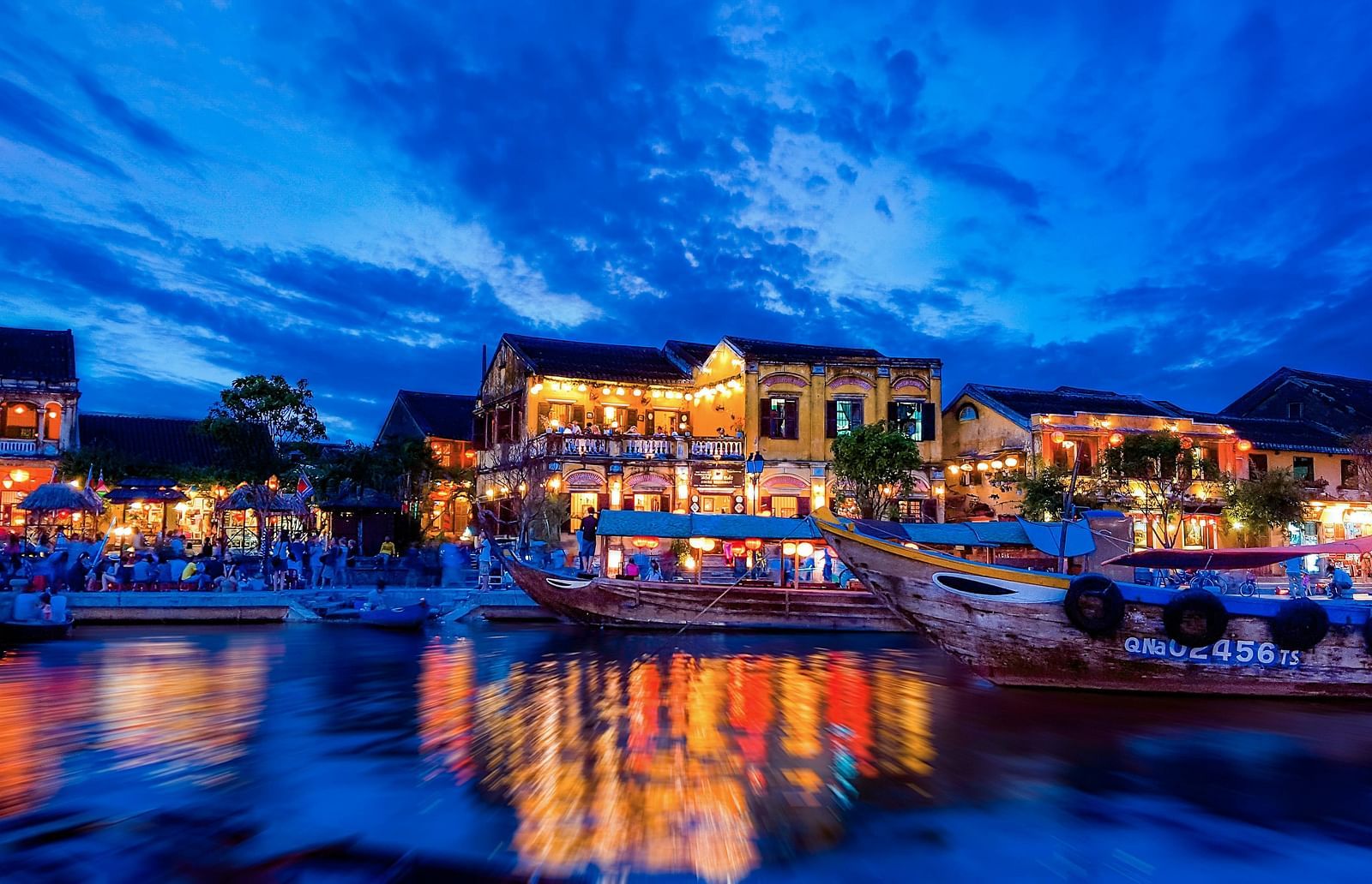 A view of boats passing by a village at night in Hoi An.