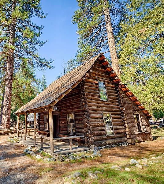 An overview of a cabin in the woods with tall trees next to it.