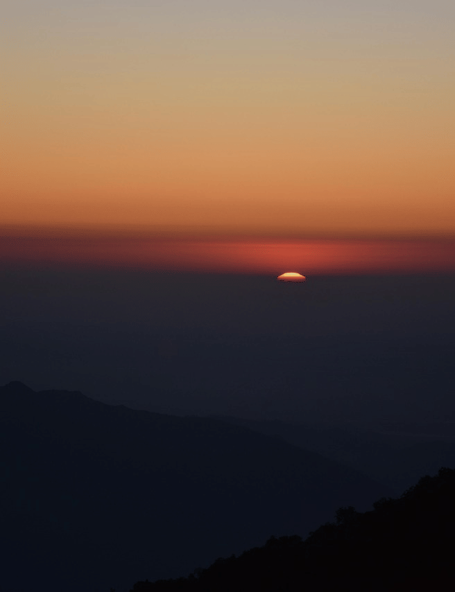 A striking sunset with a deep orange glow on the horizon over several layers of dark mountain ranges.