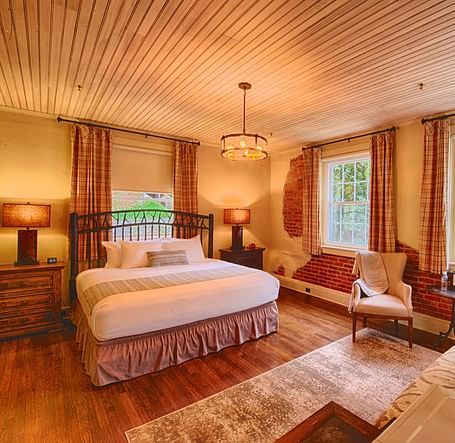 a room with ample natural lighting coming from the huge windows in the room with plush arm chairsa brightly lit bathroom featuring a door opening to the bedroom overlooking the double bed - Historic Tapoco Lodge