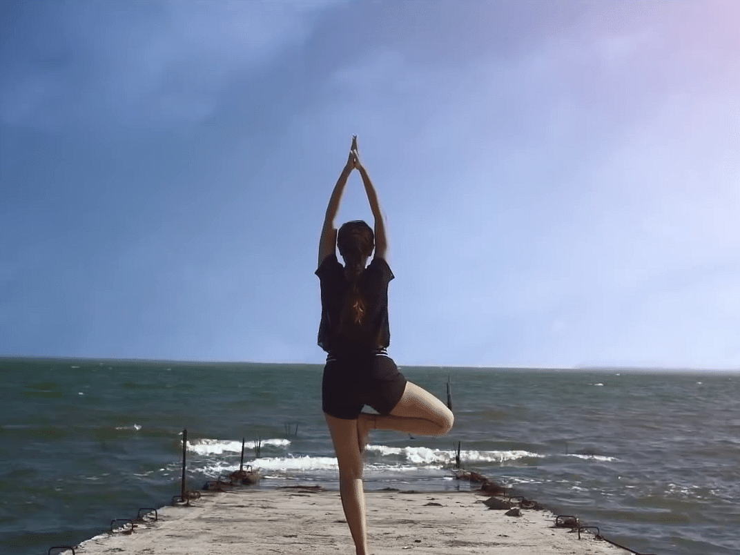 A person doing yoga at a beach on a clear, blue day