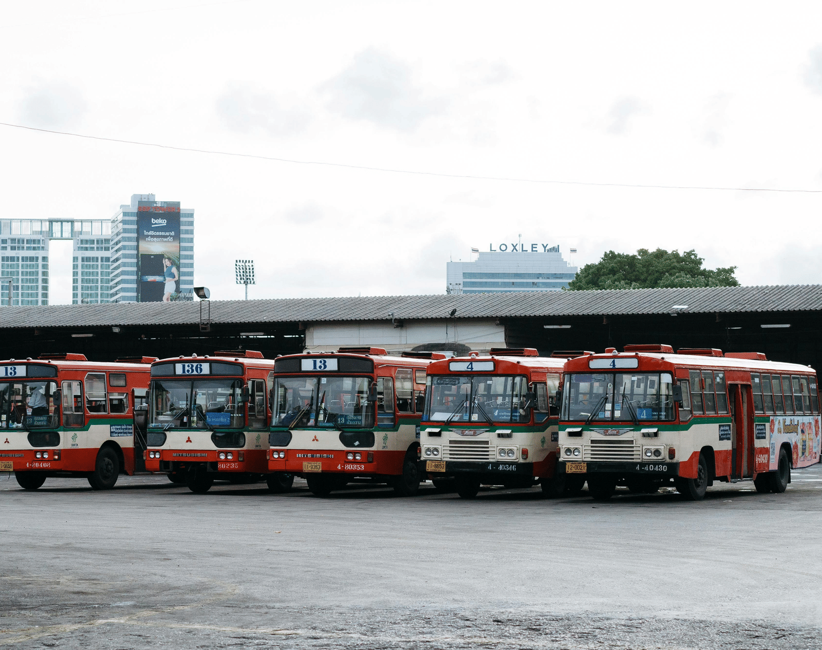 A bus depot with 5 busses parked together closely.