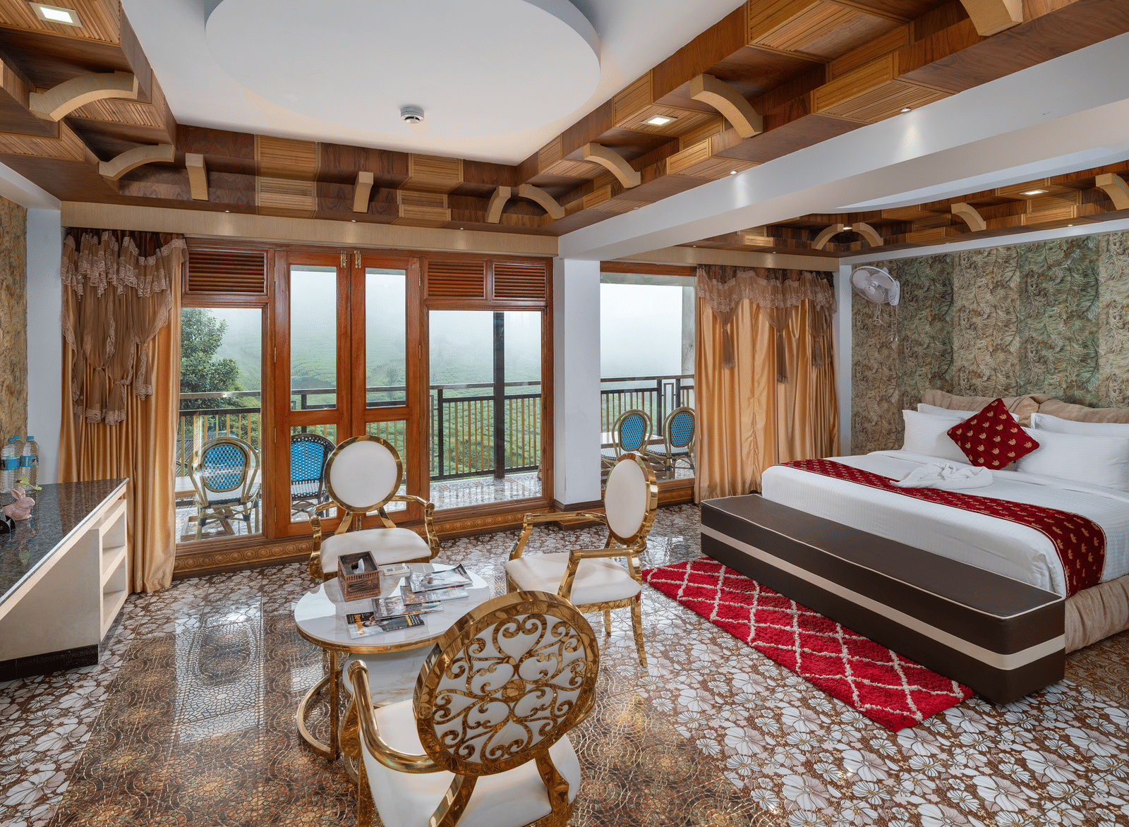 The expansive bedroom of the Presidential Suite at Parakkat Nature Hotel and Resorts, Munnar, featuring a large bed, decorative wooden-beam ceilings, a seating area with a table, and glass doors opening to a scenic view.