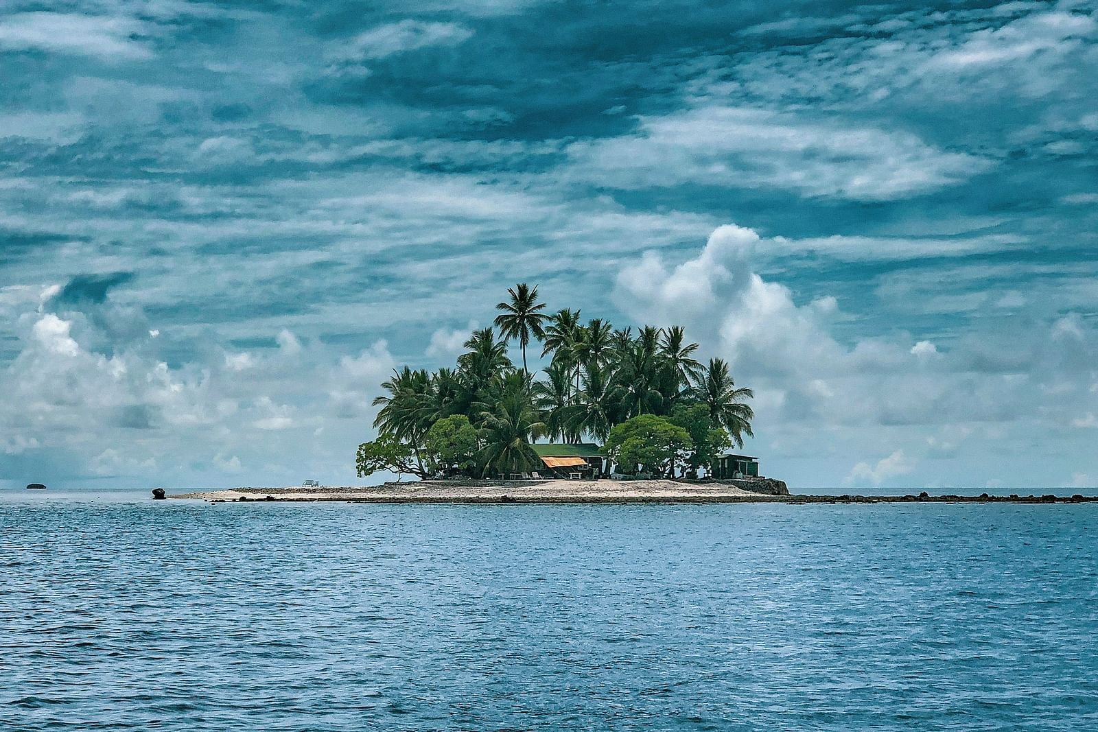 an island in the middle of an ocean with trees on top of it and white clouds on blue sky in the background