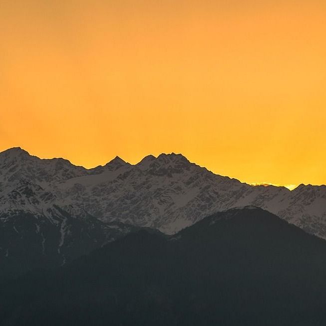 the bright yellow light of the sun shining behind mountains