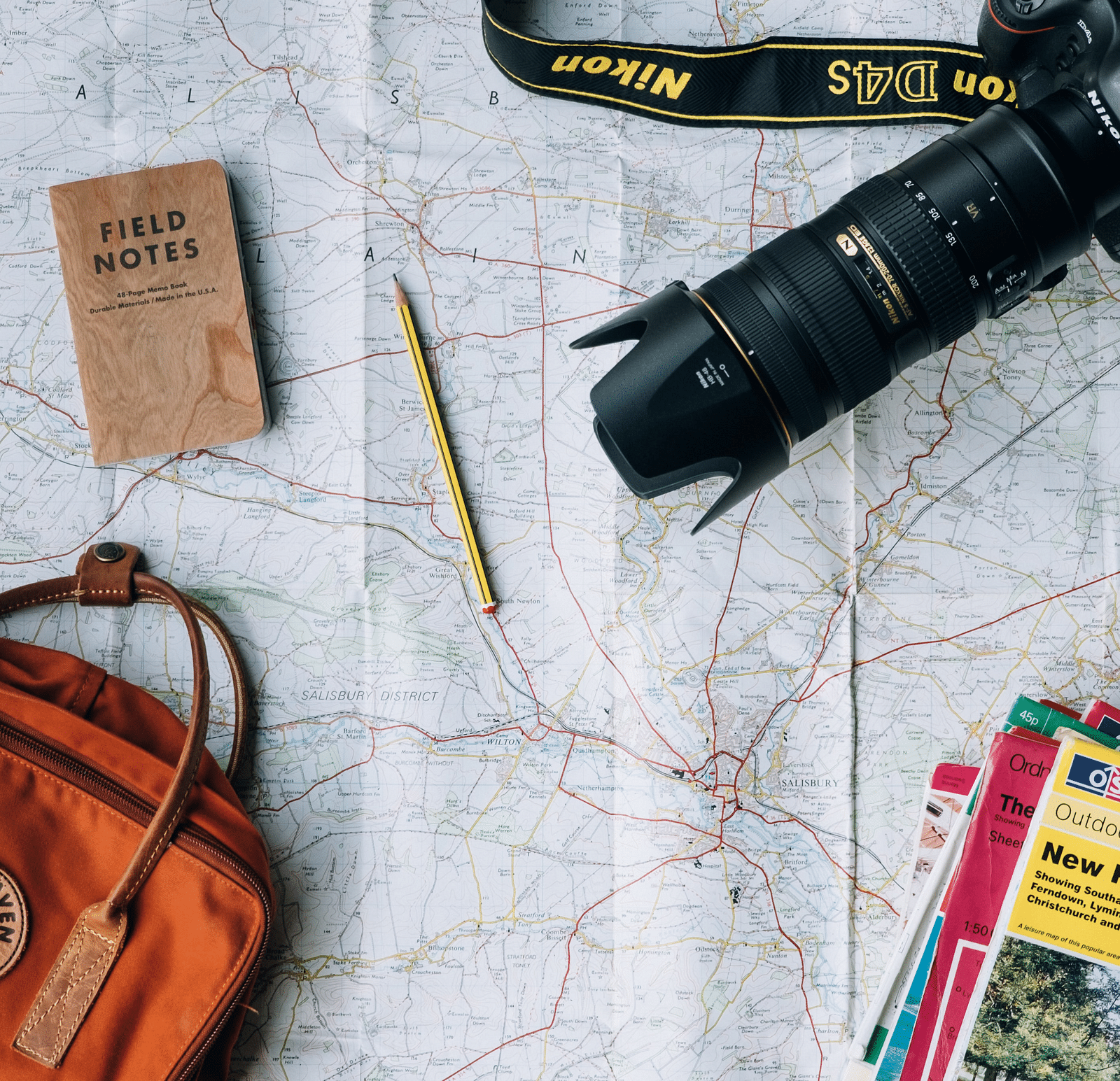 A picture of a camera, a few magazines, a handbag, a diary, and a pencil arranged on a map.