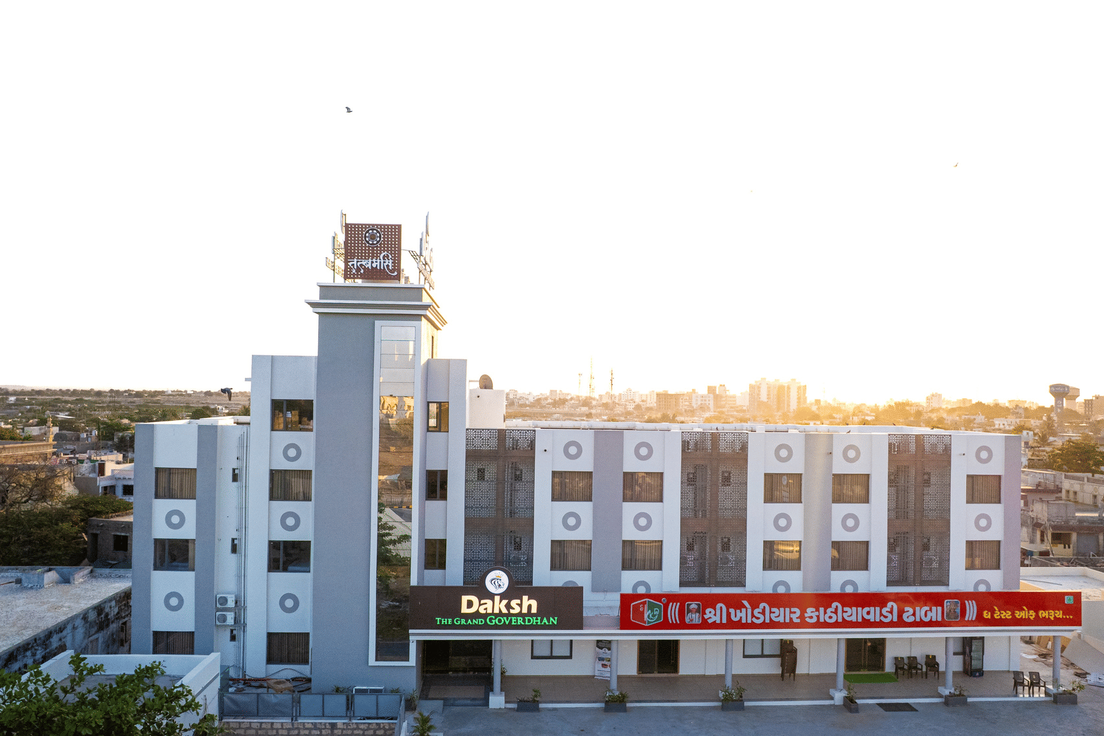 Front view of Daksh The Grand Goverdhan, Dwarka, bathed in the morning light, showcasing its modern architecture and entrance.