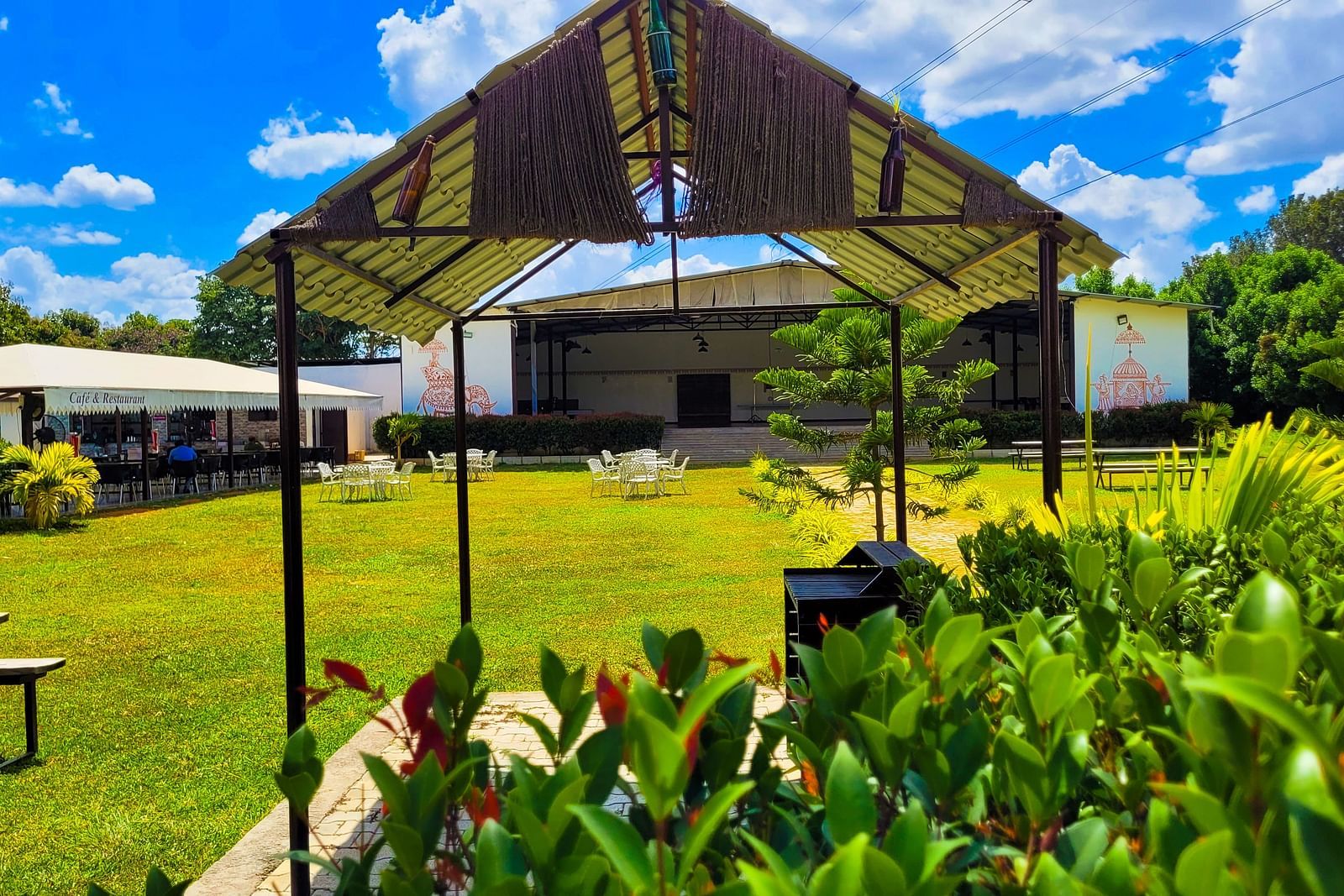 Covered area with tables lined under a beige canopy amidst lush greenery. | Vistar Resort, Bengaluru
