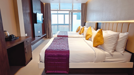 2 beds with purple runners face a large window and balcony door in a hotel room at Bliss Casa Mila By Bergamont Hotels, Kodaikanal.