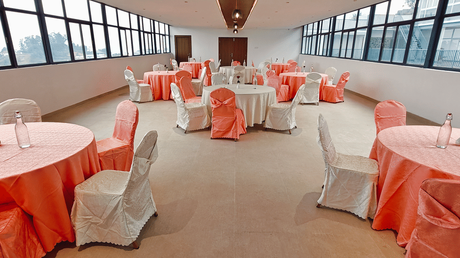 Round tables with peach and white covers and chairs are arranged in a spacious hall at Bliss Casa Mila By Bergamont Hotels, Kodaikanal.